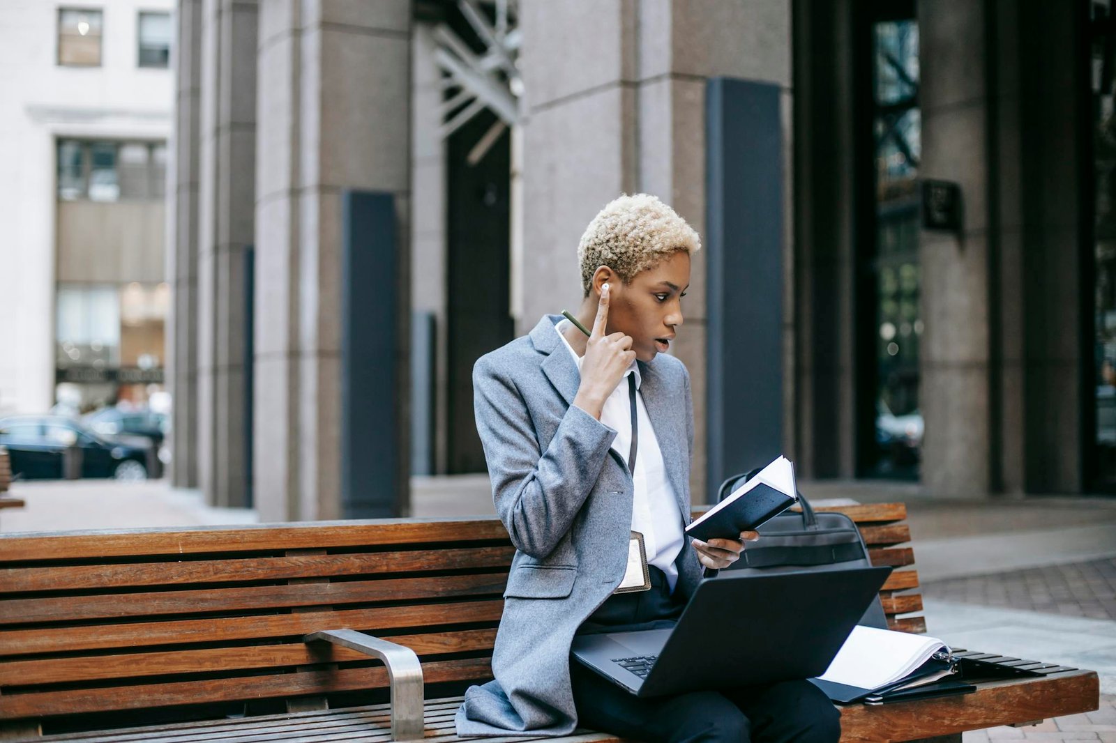 Concentrated self employed female entrepreneur working remotely while sitting with laptop and papers near urban building in daytime