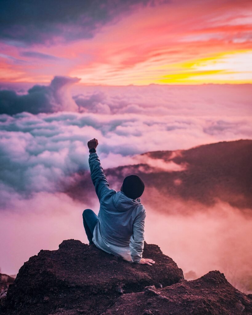 a person sitting on a rock with a sunset in the background