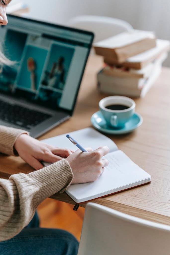 Businesswoman writing thoughts in empty notebook near laptop and coffee