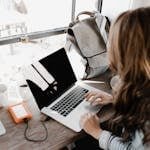 Close-up Photography of Woman Sitting Beside Table While Using Macbook