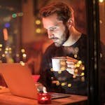 Man Holding Mug in Front of Laptop