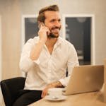 Smiling formal male with laptop chatting via phone